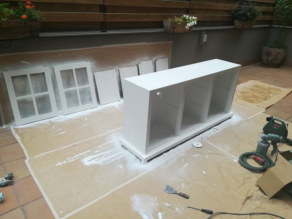 Maqueta de armario blanco sobre una lona en un área de trabajo al aire libre con puertas y herramientas cerca.
