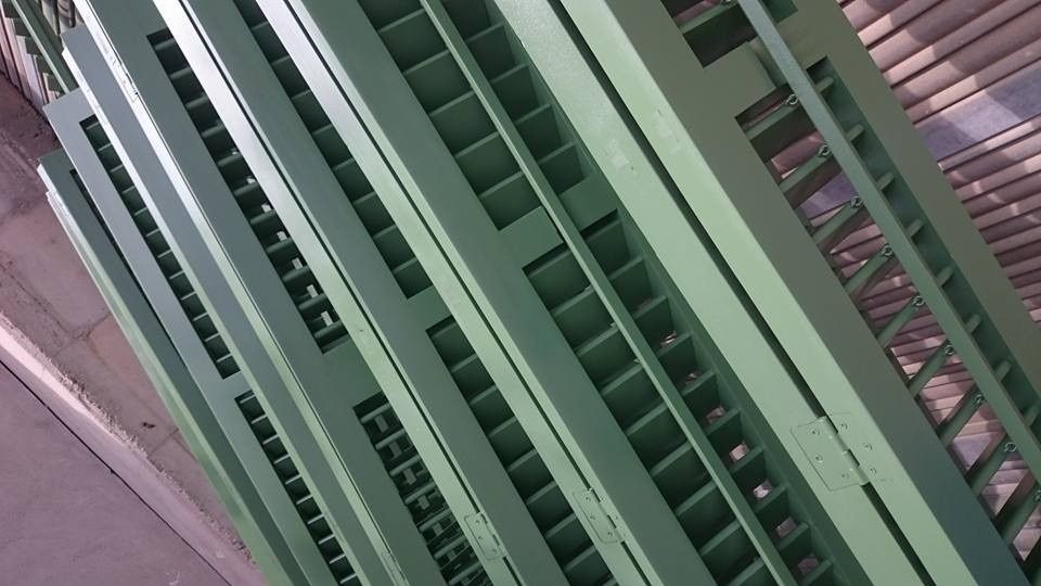 Primer plano de listones o contraventanas de metal verde con una pared gris y una superficie rosa al lado.