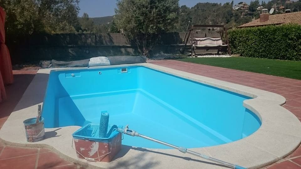 Piscina en el patio trasero con agua azul brillante, patio y árboles bajo un cielo despejado.