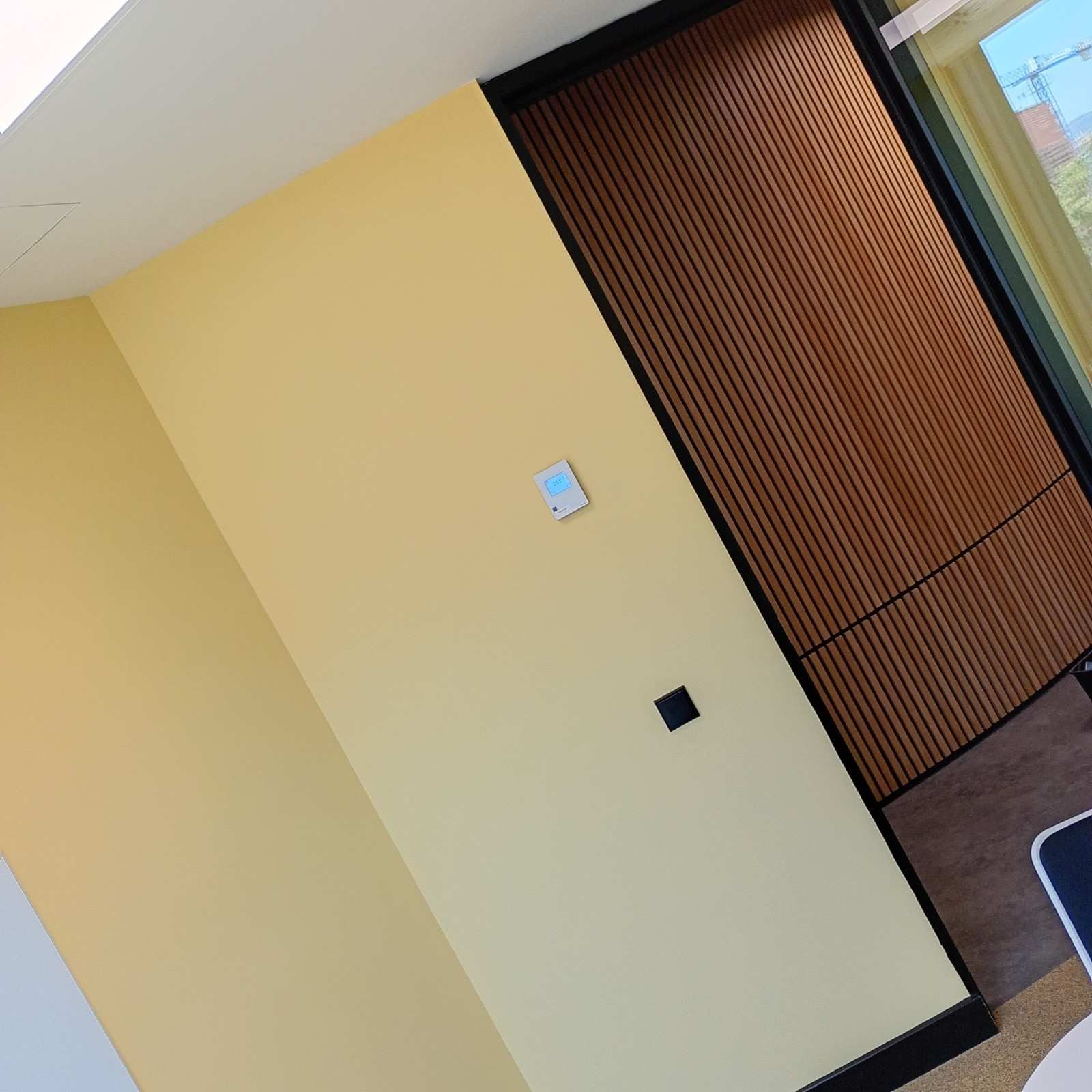 Pasillo inclinado con paredes amarillas, revestimiento de madera y un panel de control montado en la pared.