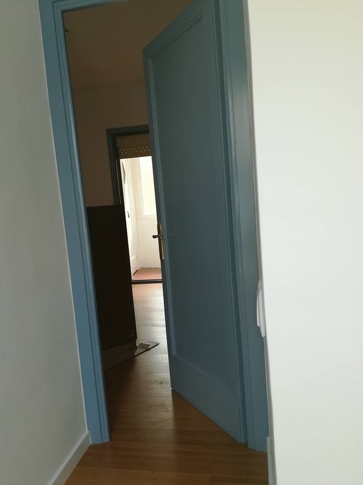 Pasillo estrecho con puertas azules abiertas que dan a una habitación soleada.