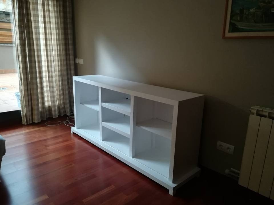 Estantería blanca en una habitación soleada junto a una ventana y un radiador, sobre un suelo de madera noble.