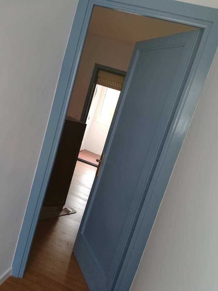 Una puerta azul da acceso a un pasillo con una habitación luminosa al fondo.