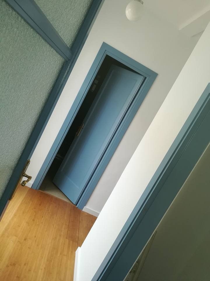 Vista inclinada de un pasillo con puertas azules, paredes blancas y suelo de madera.