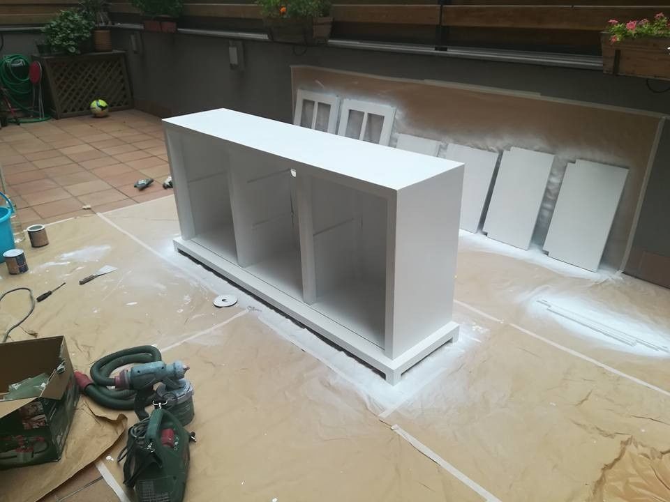 Un armario o estantería blanca está siendo pintado en un taller con herramientas y tablones cerca.