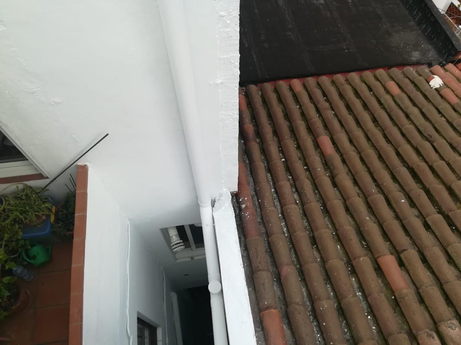 Un trabajador pinta un mural en una pared bajo un andamio, con casco blanco y guantes.