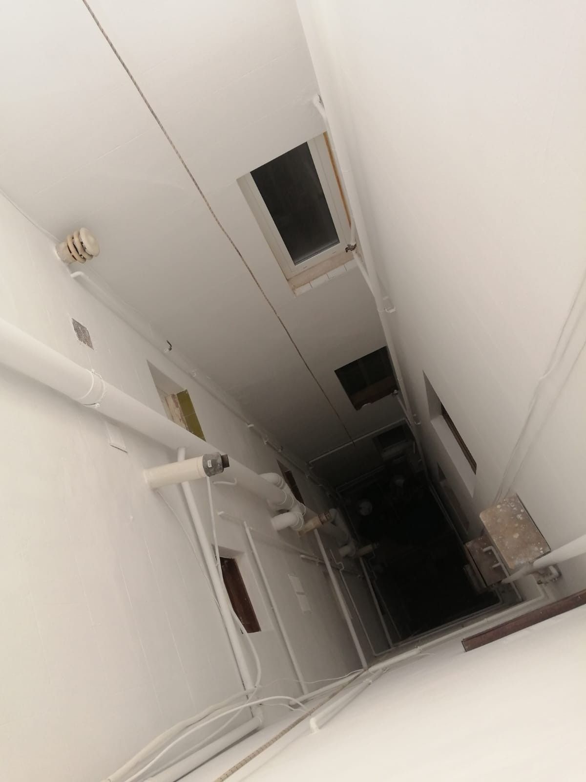 Vista inclinada hacia arriba de un pasillo blanco con rejillas de ventilación