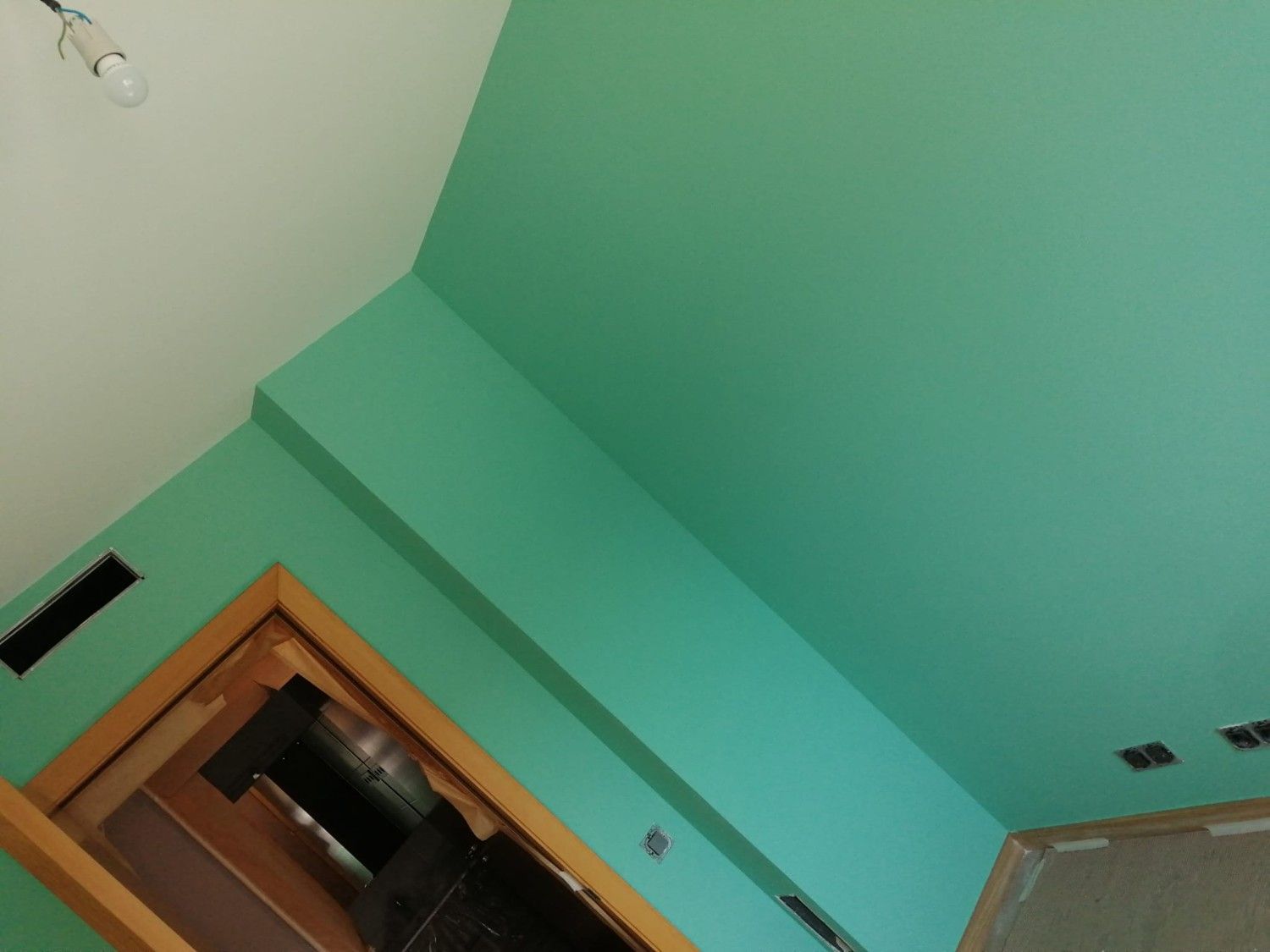 Vista inclinada de una habitación turquesa con una puerta de madera y techo blanco.