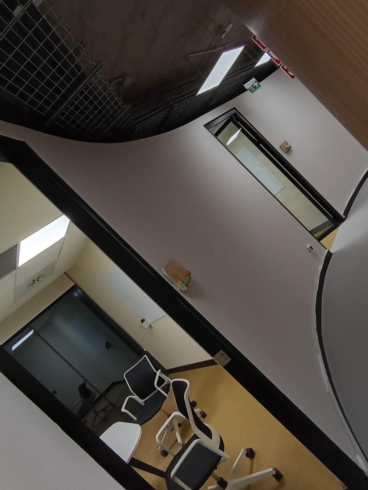 Vista inclinada del vestíbulo de una oficina con sillas, un escritorio, paredes de cristal y luces en el techo.