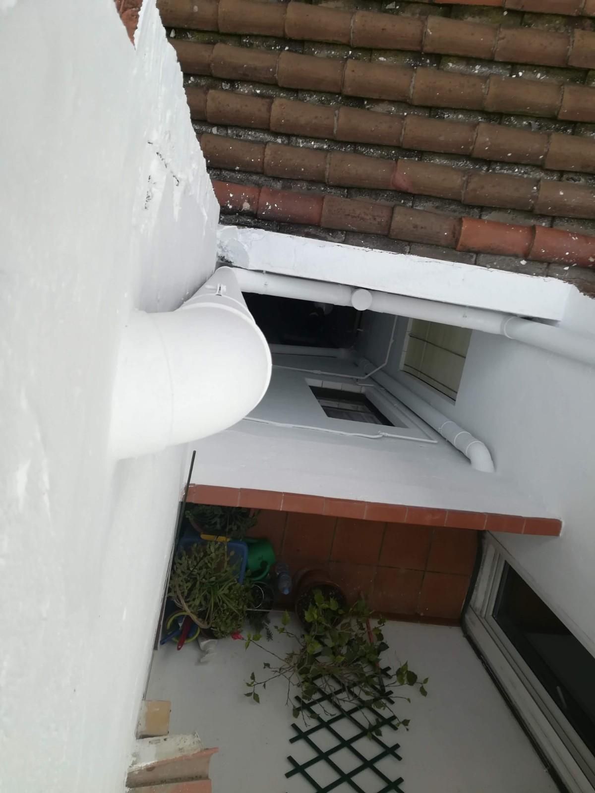 Balcón cubierto de nieve con paredes blancas, tejas marrones y un pequeño patio debajo.