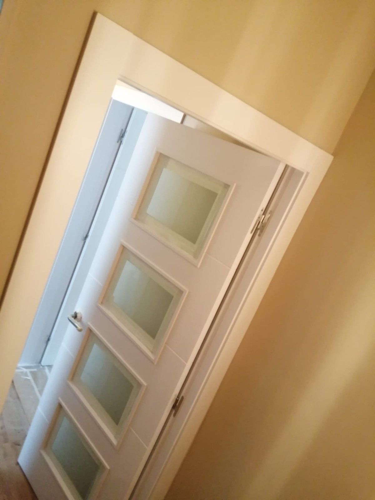 Puerta blanca con paneles de vidrio esmerilado, vista desde un ángulo en un pasillo de color beige.