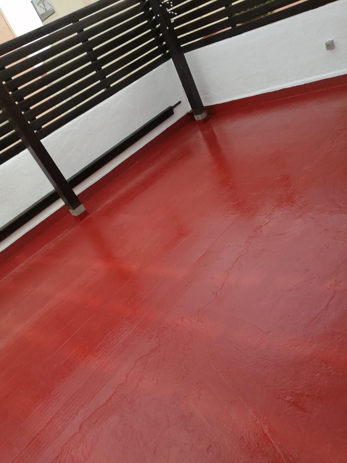 Balcón con suelo rojo, barandilla negra y pared blanca, visto desde un ángulo.