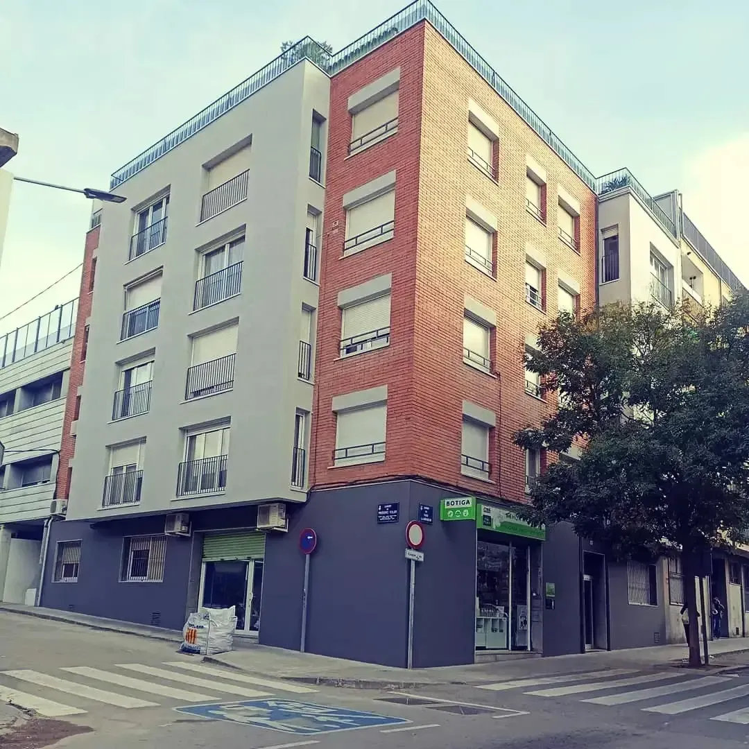 Edificio de apartamentos en esquina con fachadas de ladrillo rojo y gris en una tranquila intersección de calles.