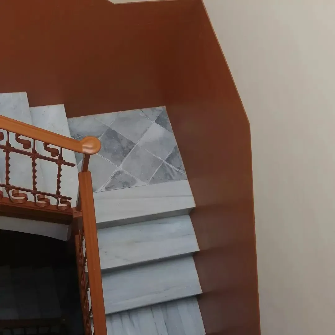 Escalera interior con barandilla de madera, pared marrón y rellano alicatado.