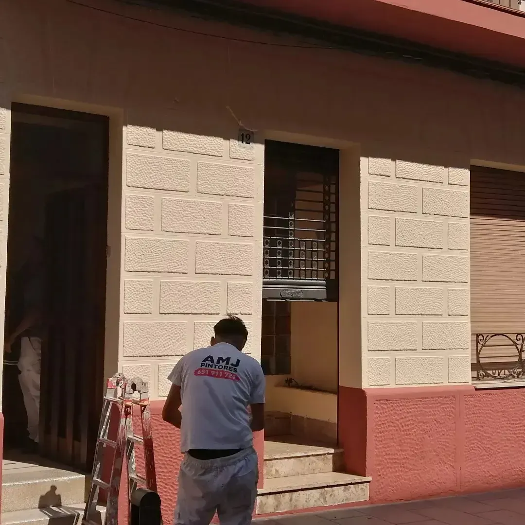 Una persona limpia las escaleras exteriores de un edificio beige con una pared inferior roja.