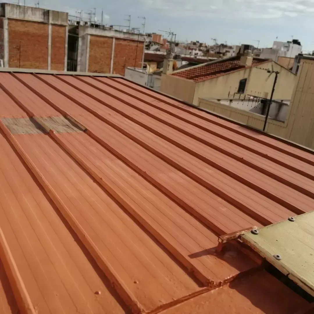 Tejado de chapa ondulada color óxido con edificios cercanos al fondo.