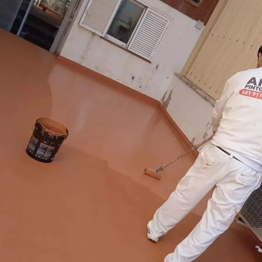 Persona con ropa de trabajo blanca usando un rodillo de pintura sobre 