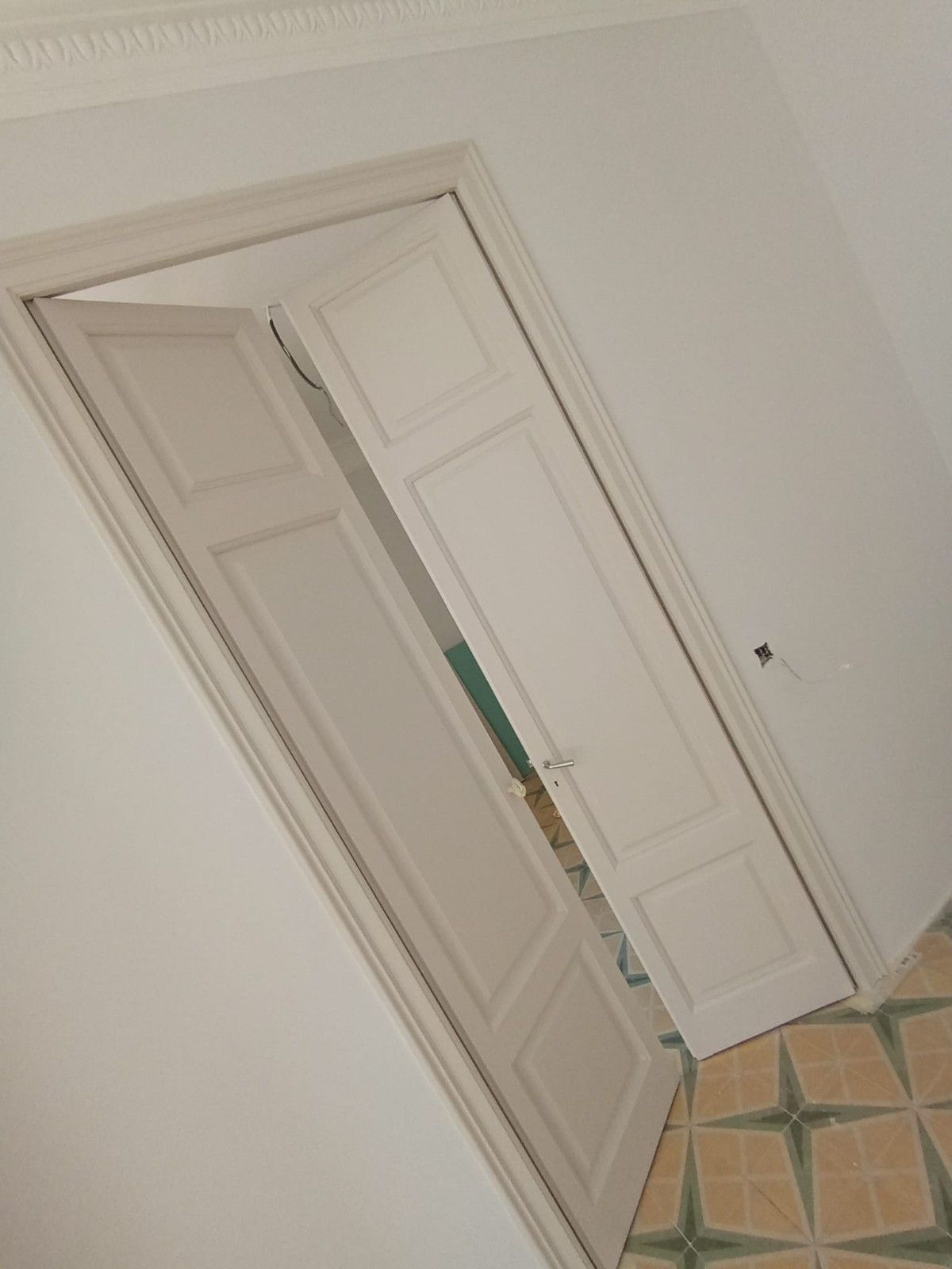 Vista inclinada de una puerta blanca con una puerta abierta y suelo de baldosas estampadas dentro de una habitación luminosa.