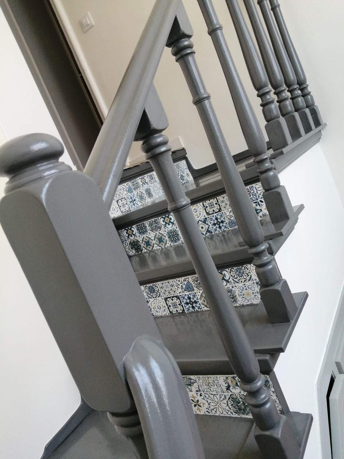 Escalera gris con barandilla ornamentada y alfombra estampada en un pasillo.