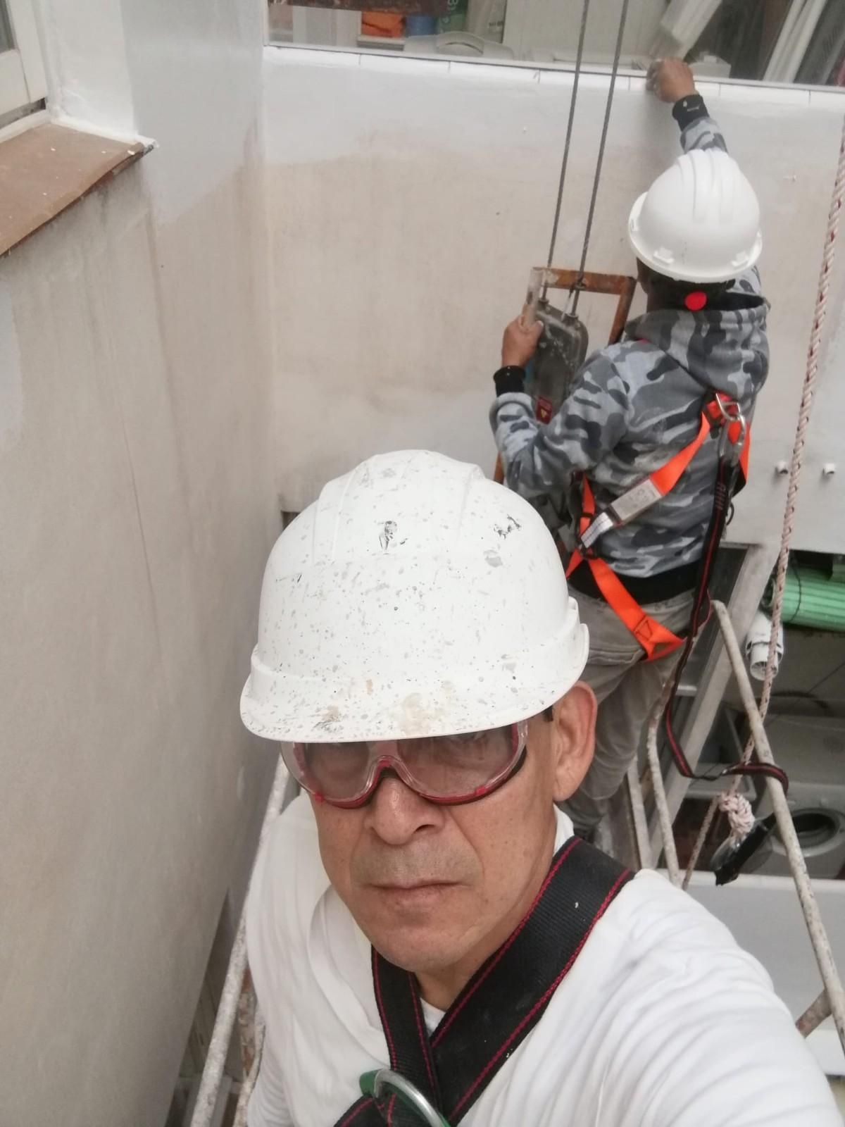 Dos trabajadores con cascos y arneses de seguridad en un andamio estrecho