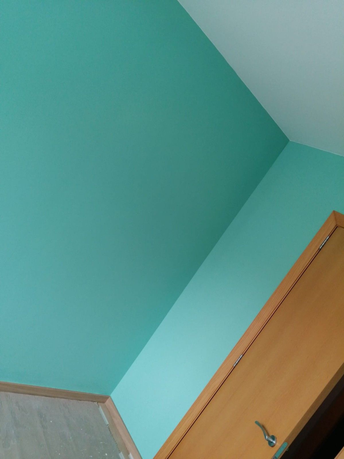 Techo y paredes de color verde azulado con una puerta de madera en la esquina de una habitación.