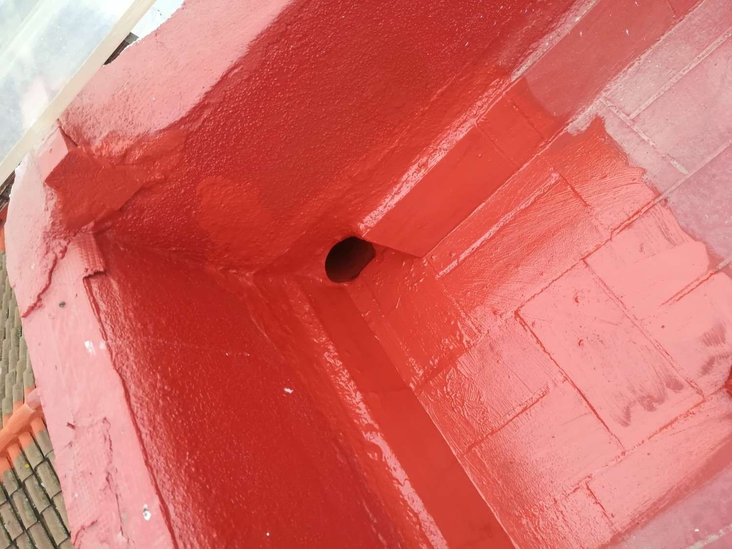 Primer plano de una superficie metálica pintada de rojo brillante con un pequeño agujero negro en el centro.