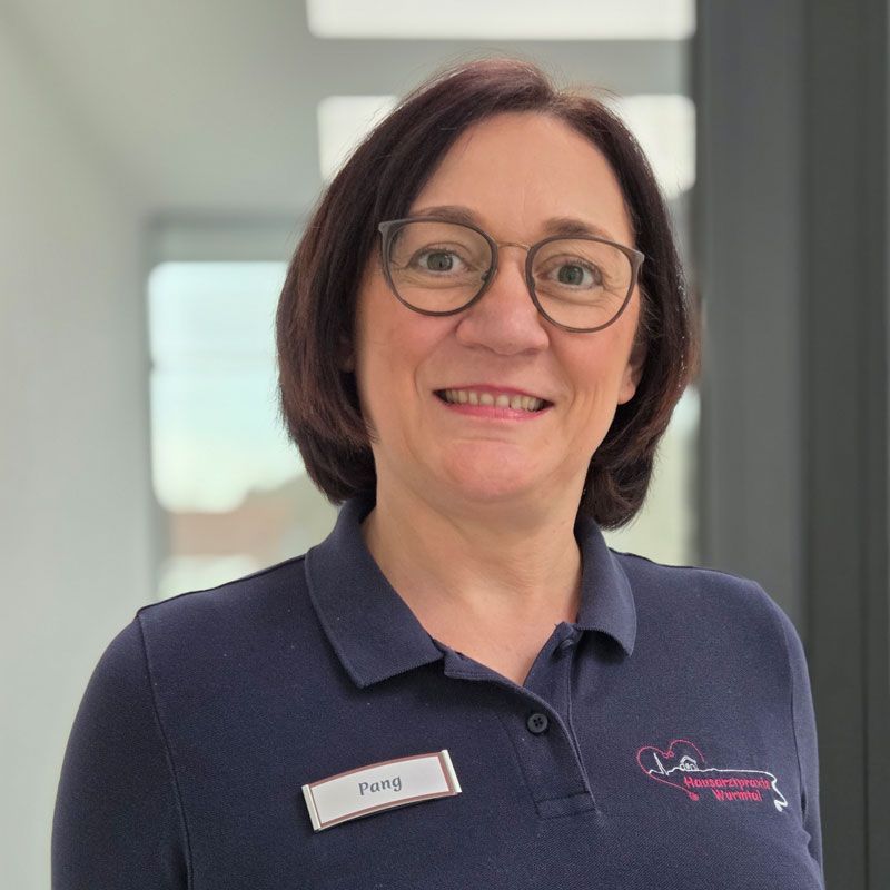 Katharina Kirwald Frau mit Brille, dunkelblauem Poloshirt und Namensschild lächelt in einem Innenraum. Manuela Pang