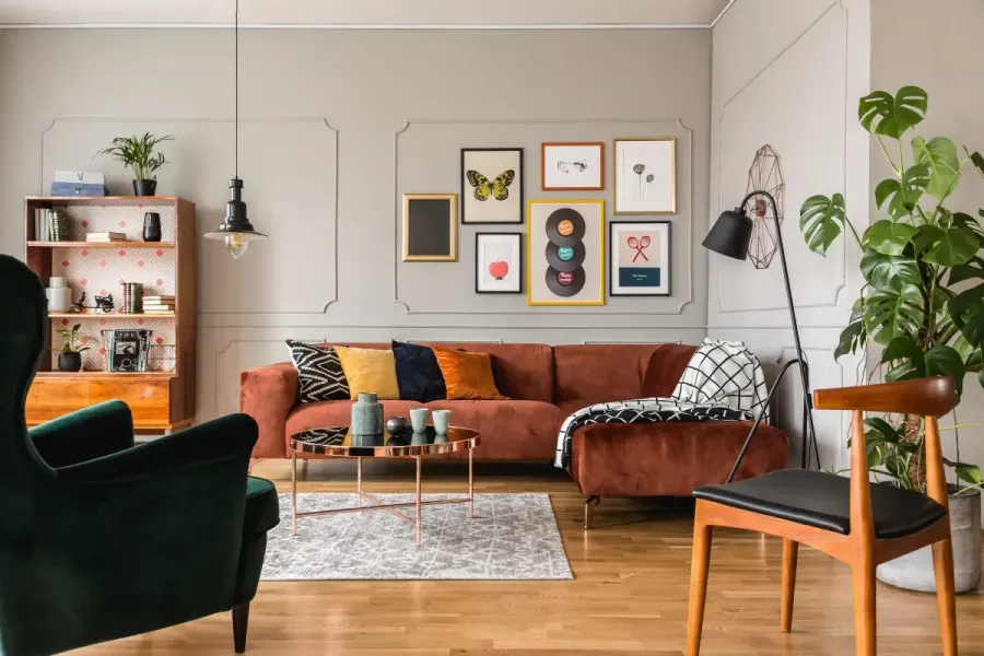 Sala de estar con sofá color óxido, pared de galería, sillón verde, plantas y pisos de madera.