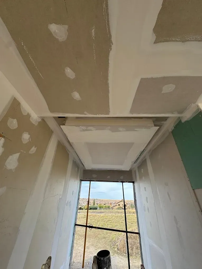 Vista de la construcción: Techo y paredes de yeso, sin terminar, con una ventana que enmarca una escena al aire libre.