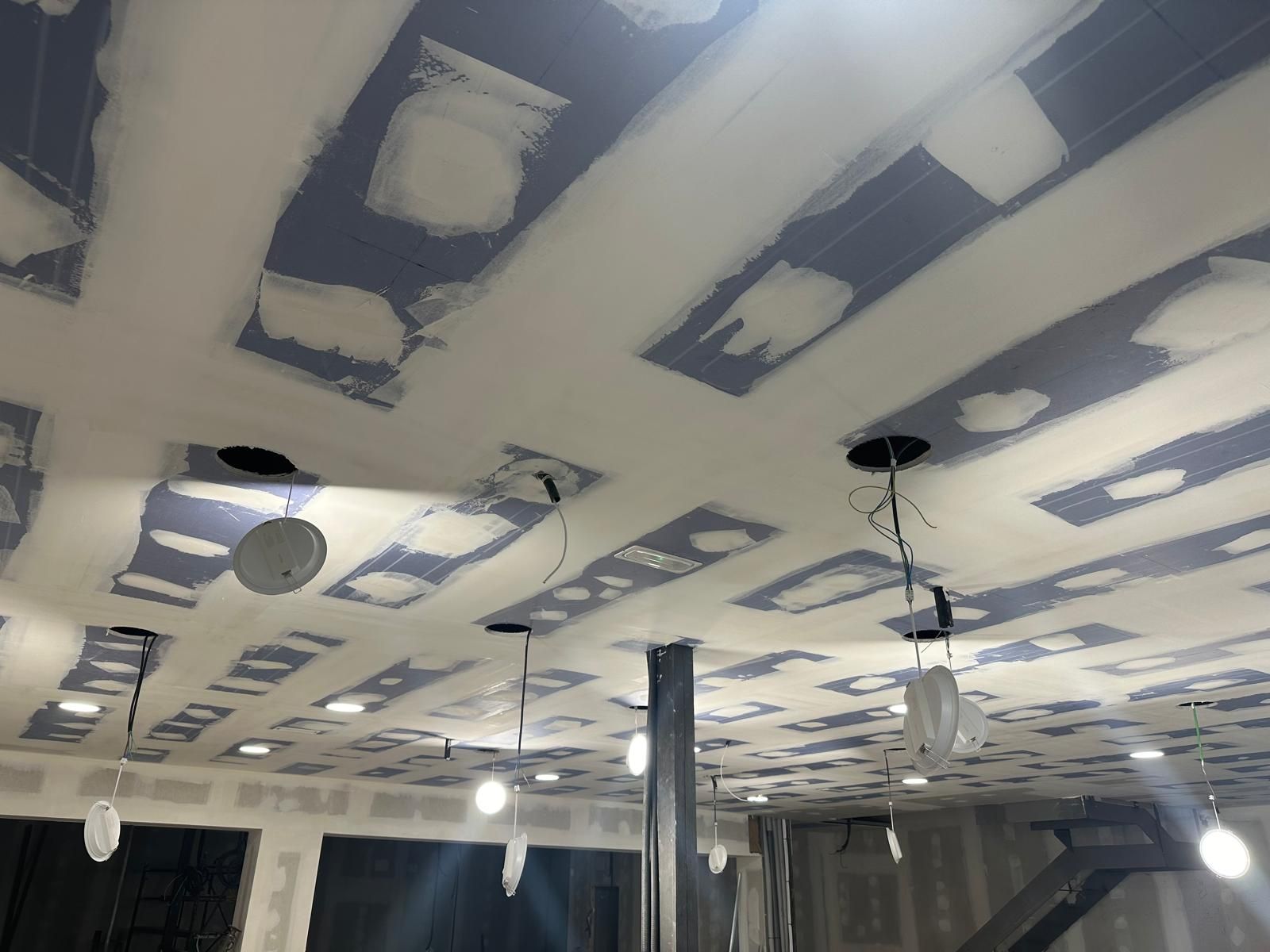 Techo en construcción con drywall y cables expuestos, luces empotradas y soporte metálico.