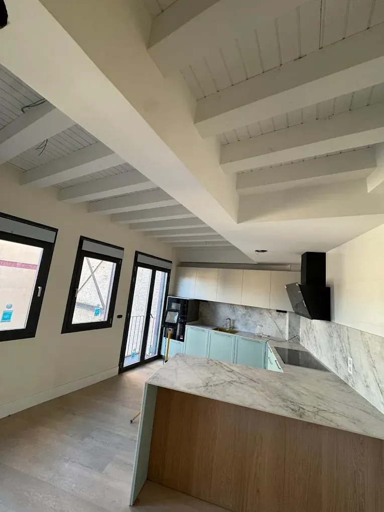 Interior de una cocina moderna con vigas de madera y encimeras de mármol.