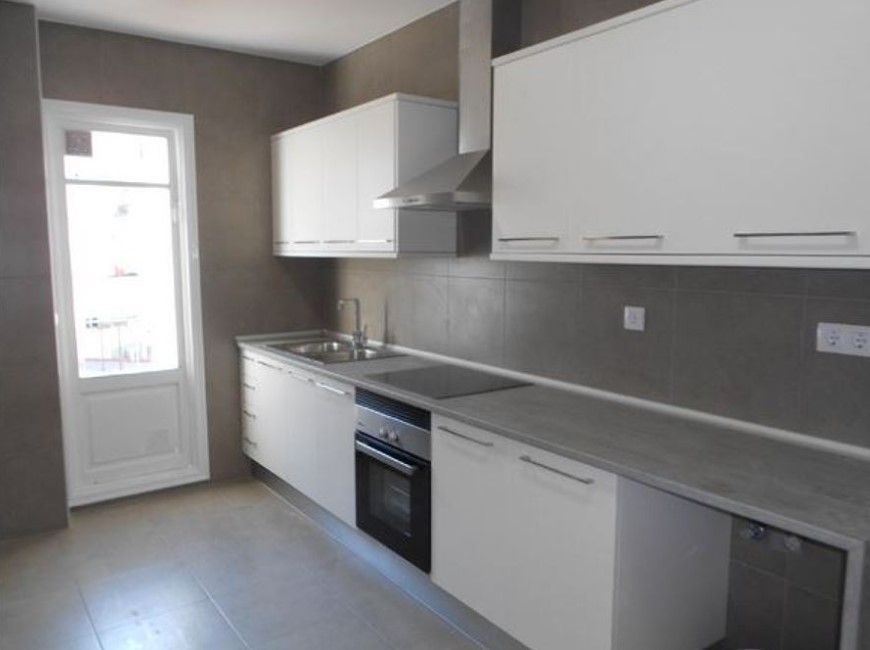 Gabinetes de cocina y encimeras de color blanco contra una pared gris, campana y puerta de acero inoxidable.