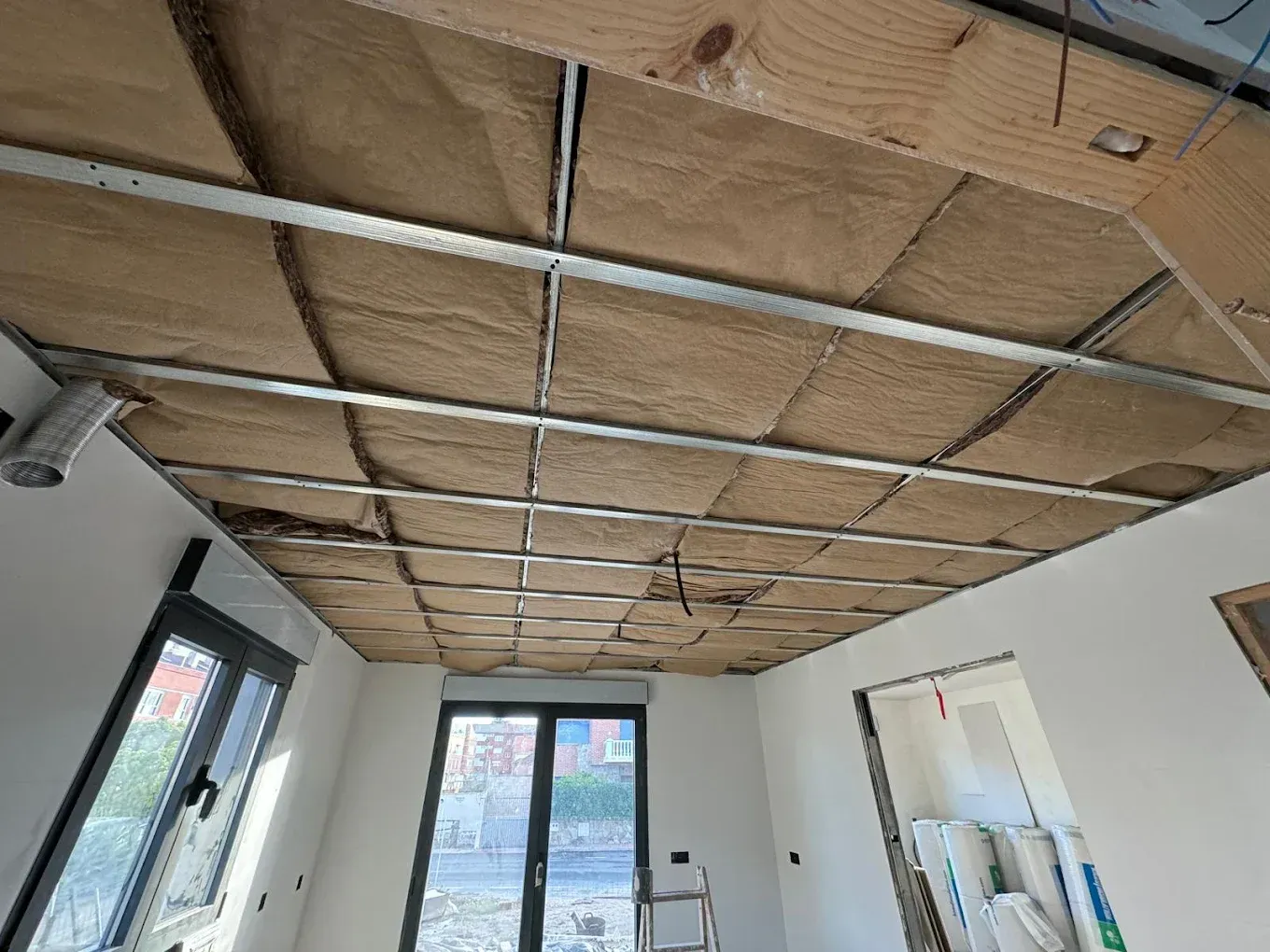 Techo en construcción con aislamiento entre rejilla metálica, ventanas y puerta visible.