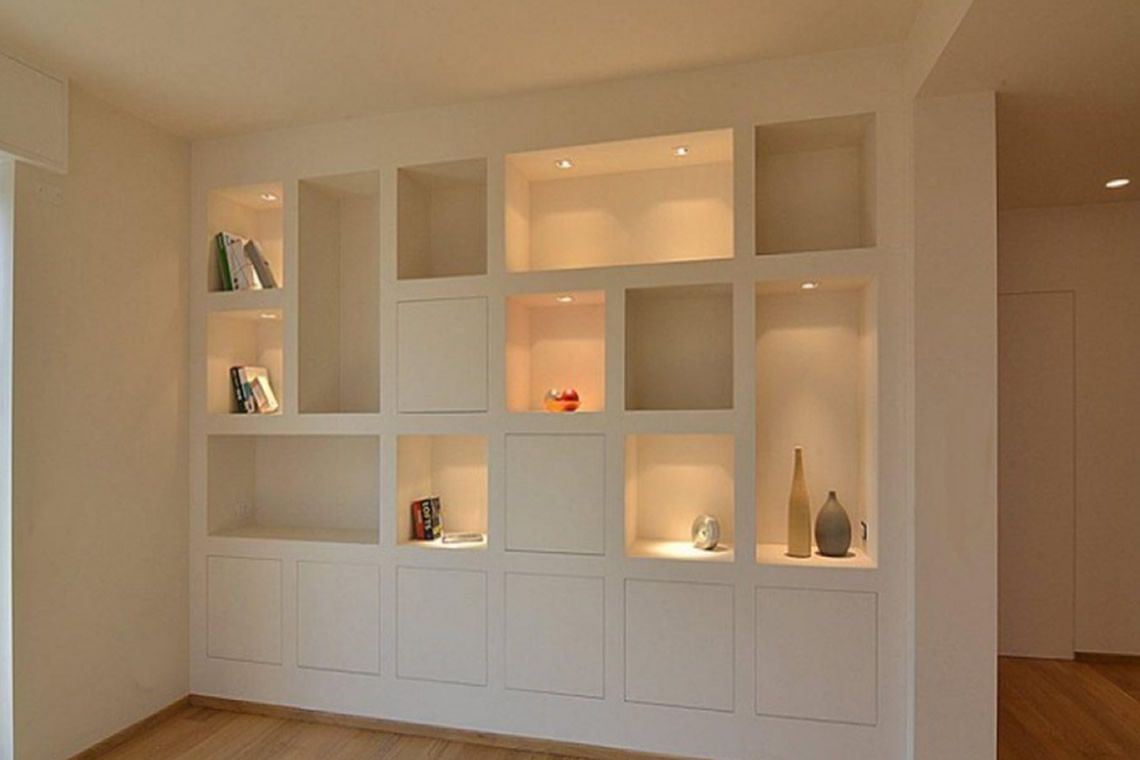 Estanterías de pared blancas empotradas con nichos iluminados que muestran elementos de decoración