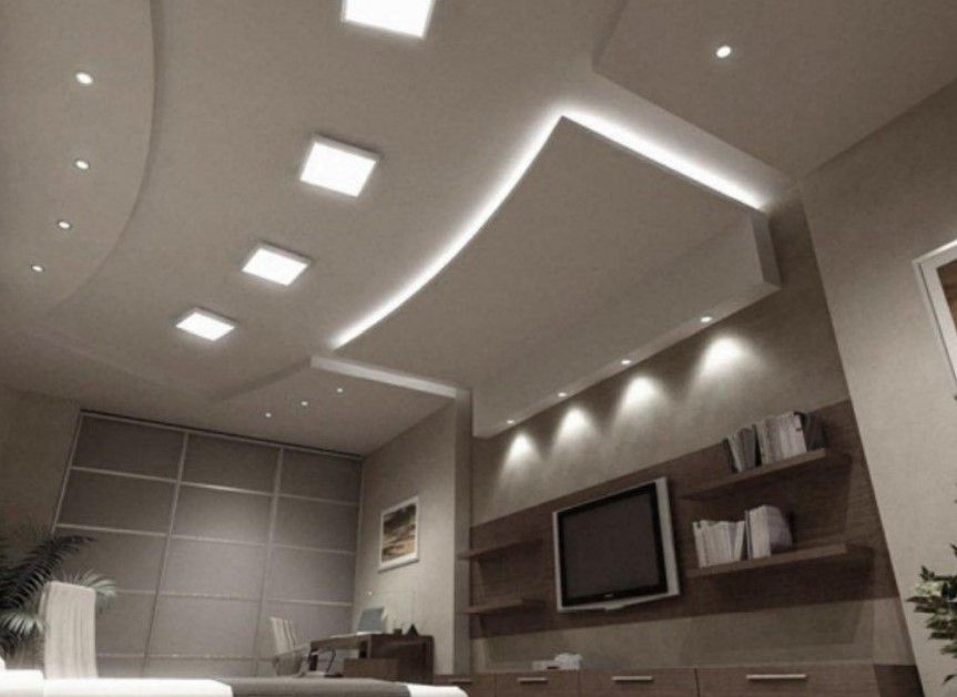 Habitación moderna con techo de varios niveles e iluminación empotrada sobre un televisor y estantes empotrados.