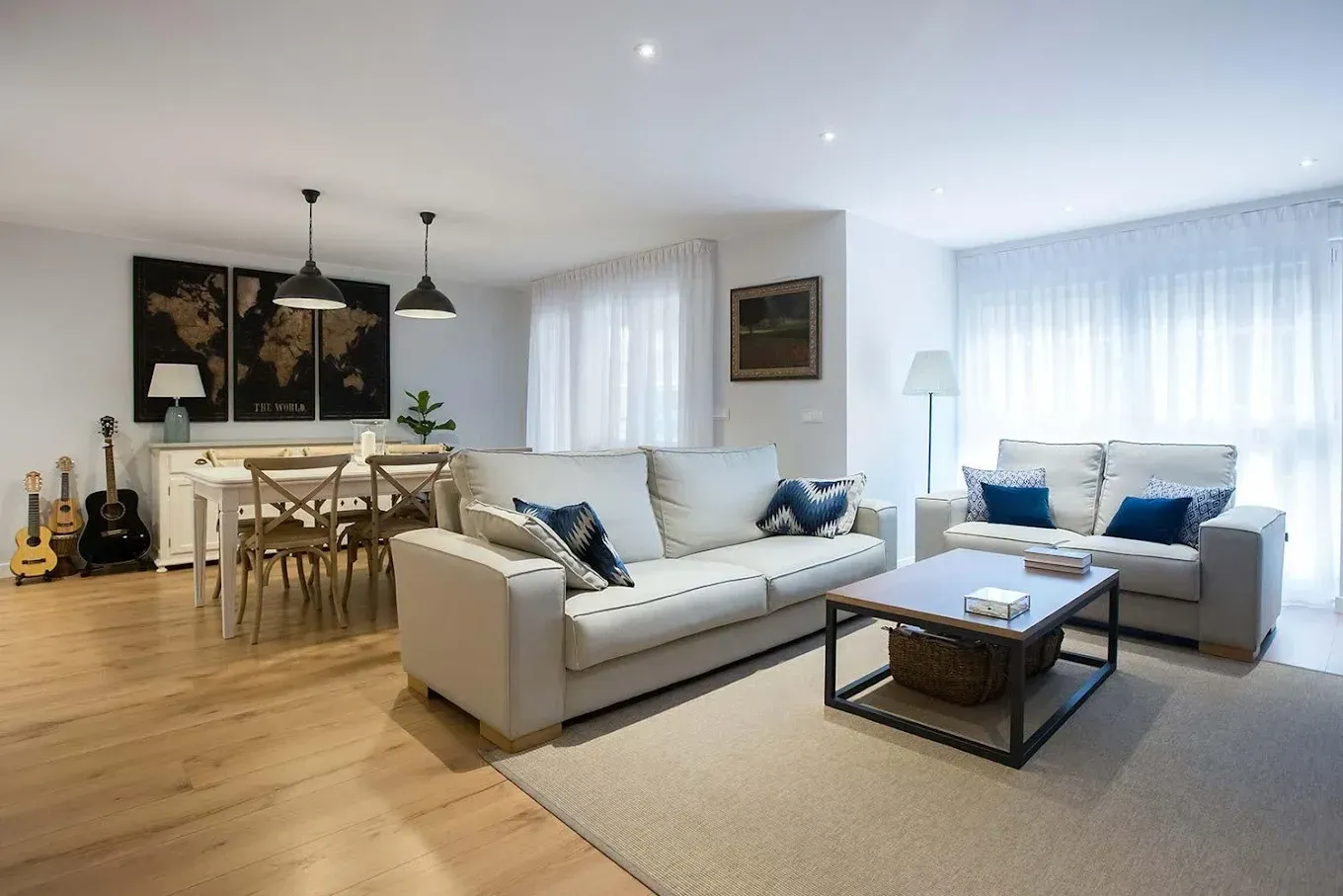 Luminosa sala de estar con sofás de color crema, pisos de madera y área de comedor; arte de mapas del mundo.