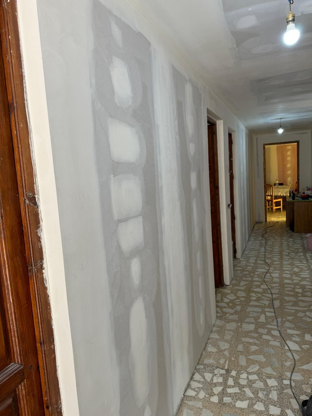 Paneles de yeso instalados en la pared de un pasillo, listos para el acabado. Vista interior con puertas y una lámpara.