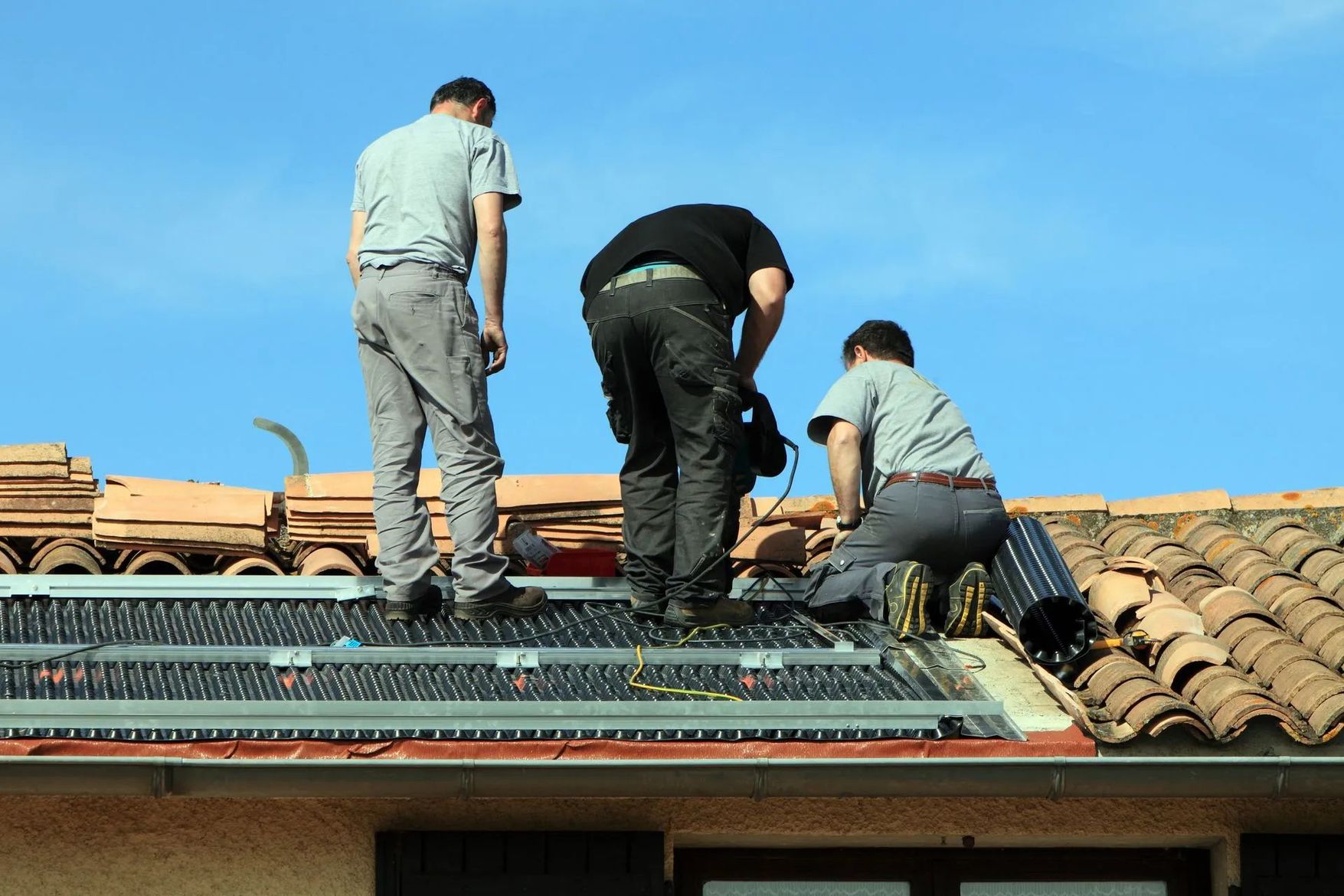 Trois couvreurs posent des tuiles sur une toiture.