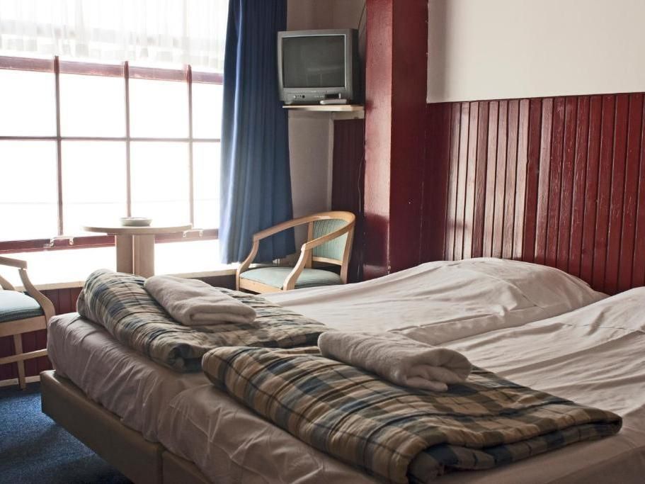 Bedroom with two twin beds, a small round table by a window, and a vintage TV. Red accent wall, blue curtains, and wooden furniture.