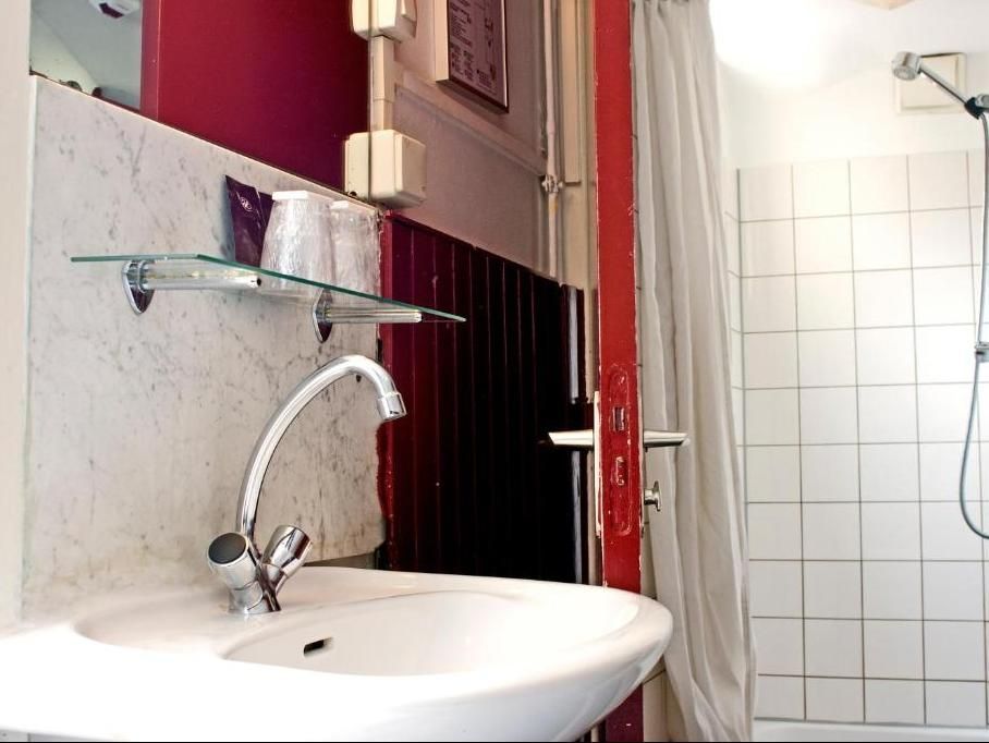 A bathroom with a sink, mirror, and shower. White sink, tiled shower, and red wall accents.