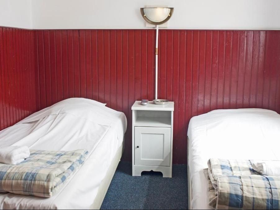 Two twin beds with white bedding, a small white nightstand, and a lamp against a red paneled wall.