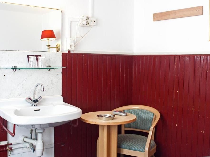 Small, red-paneled room with a sink, round table, and chair. A red lamp sits on a marble shelf.