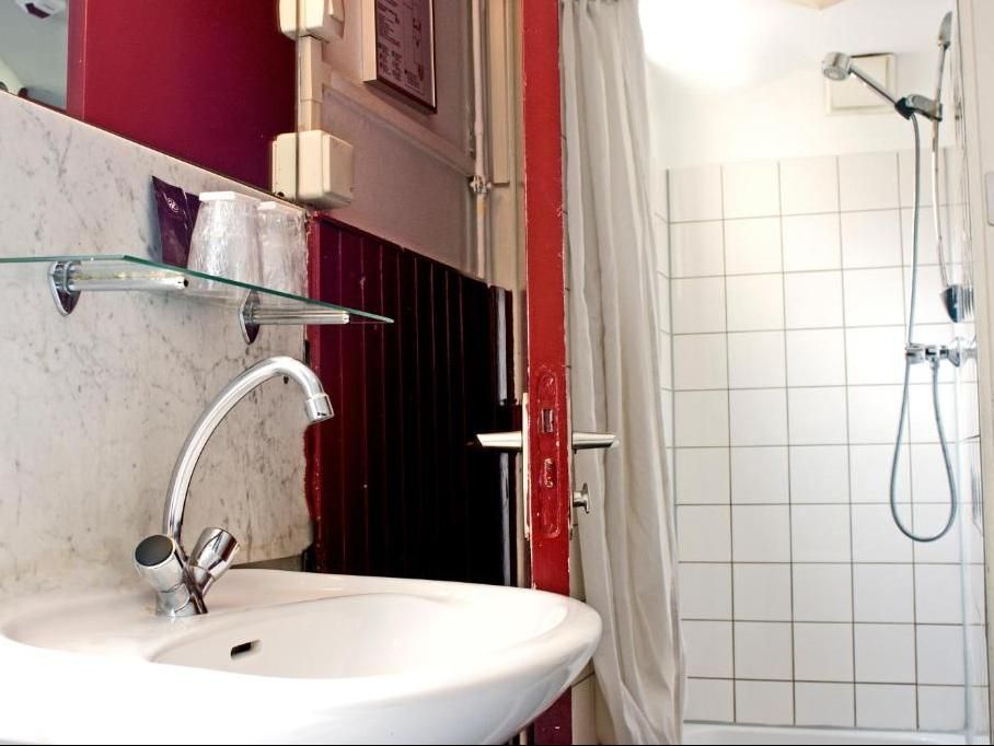 Small bathroom with a white sink, shower, and tiled walls. A red trim contrasts with the white and purple accents.
