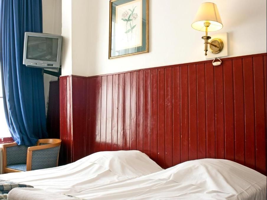Two beds with white sheets in a room with red paneling, a wall-mounted TV, and a blue curtain.