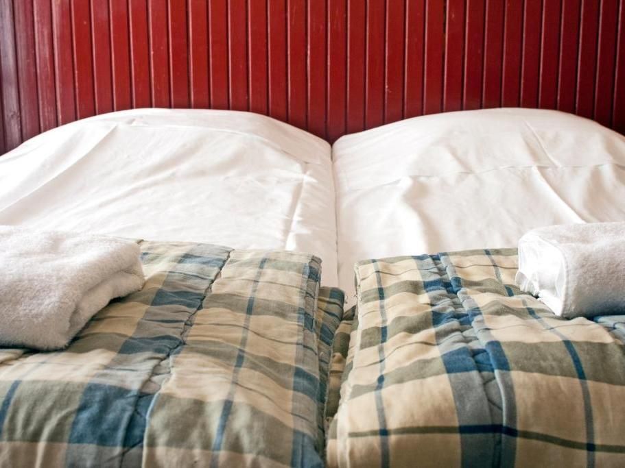 Two twin beds with white linens, plaid blankets, and rolled white towels, set against a red-slatted headboard.