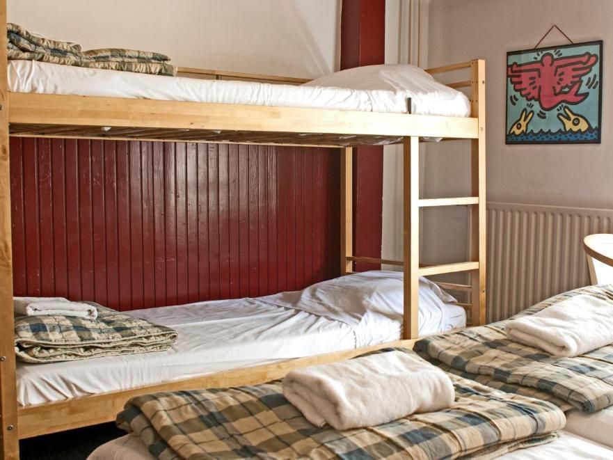 Bunk beds and twin beds in a room with a red wall and a piece of art. Several plaid blankets are visible.