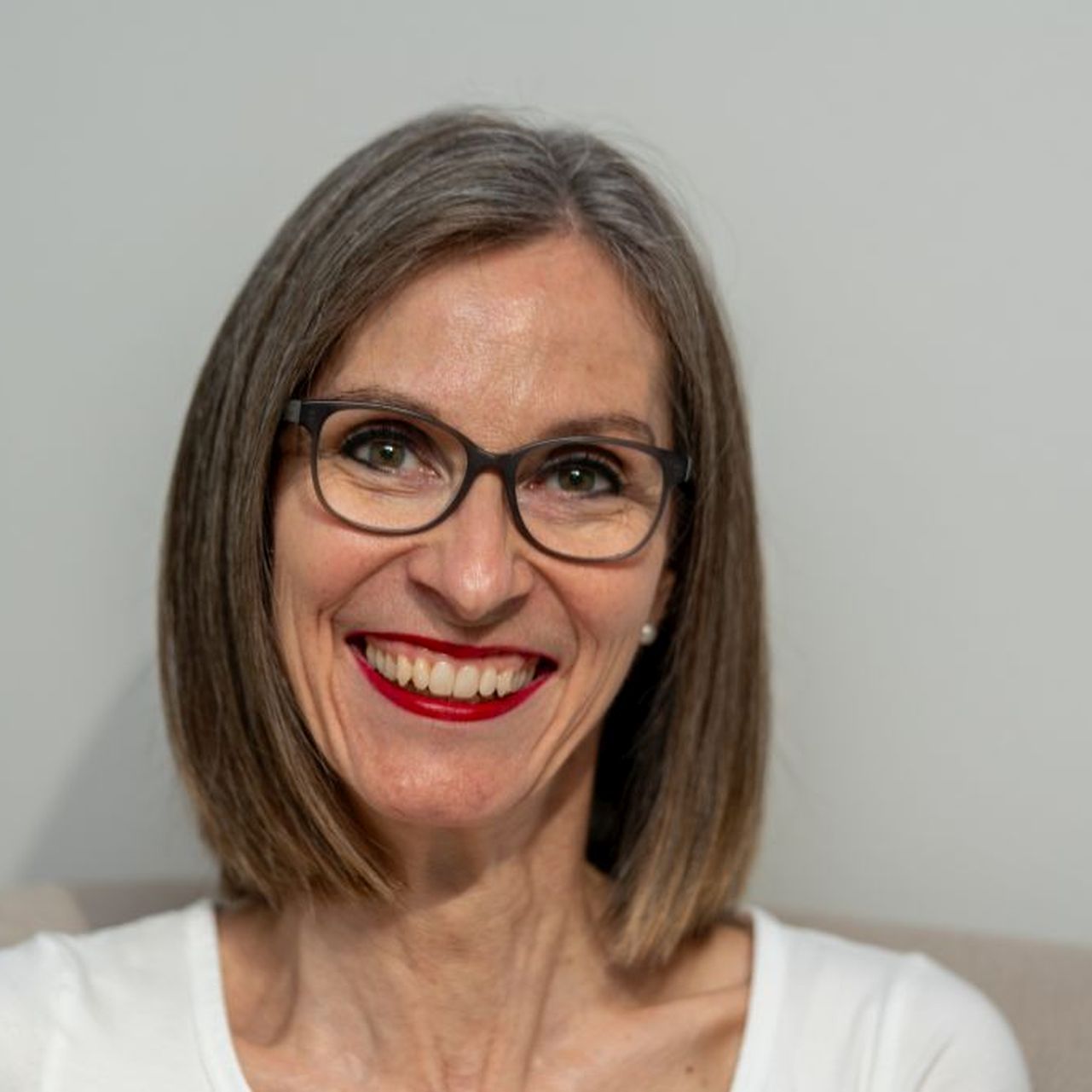 Eine Frau mit Brille und rotem Lippenstift lächelt in die Kamera.