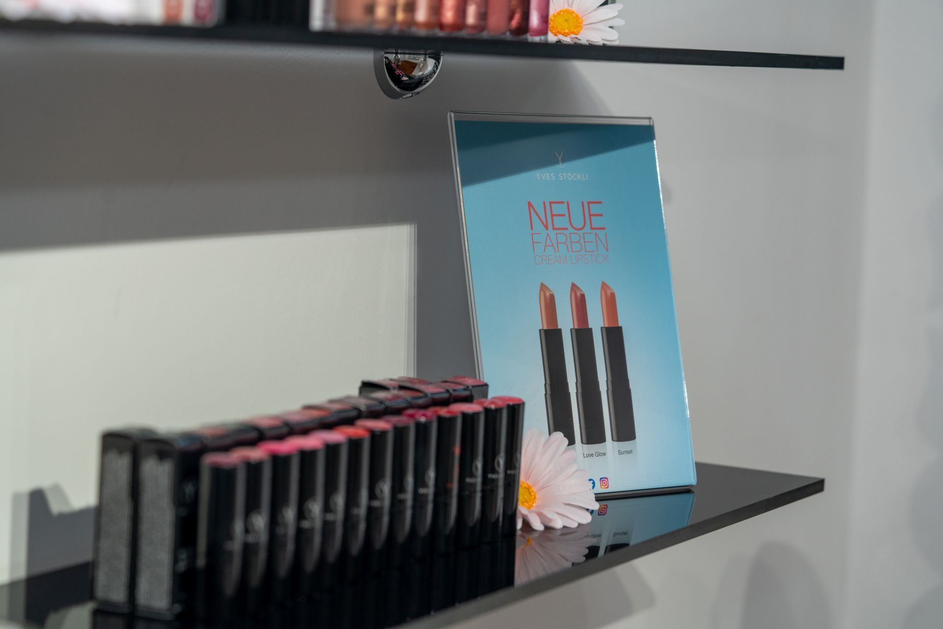 Eine Reihe Lippenstifte auf einem Regal neben einem Schild mit der Aufschrift „Neue“