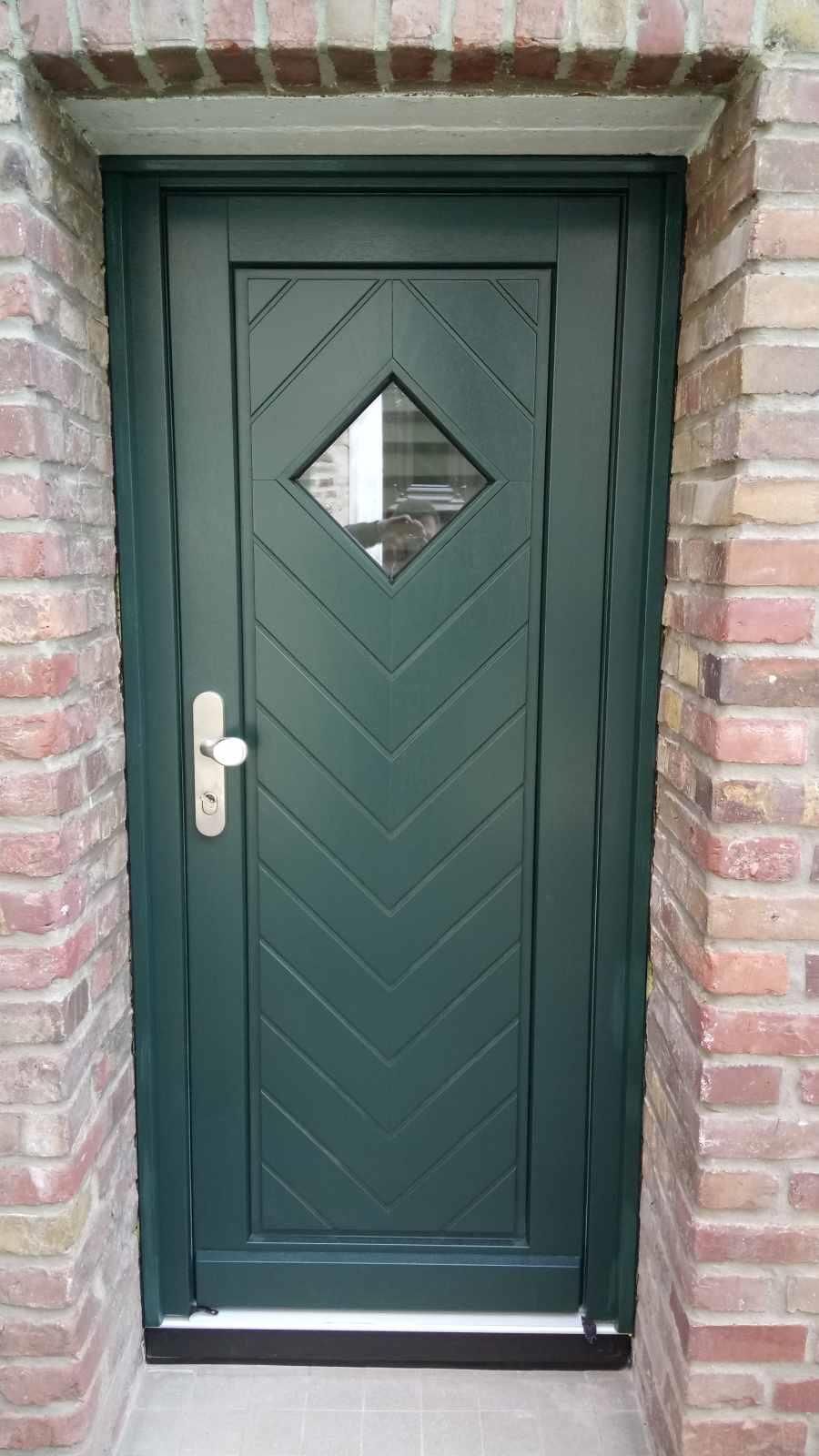 An einer Backsteinmauer befindet sich eine grüne Tür mit einer Raute in der Mitte.