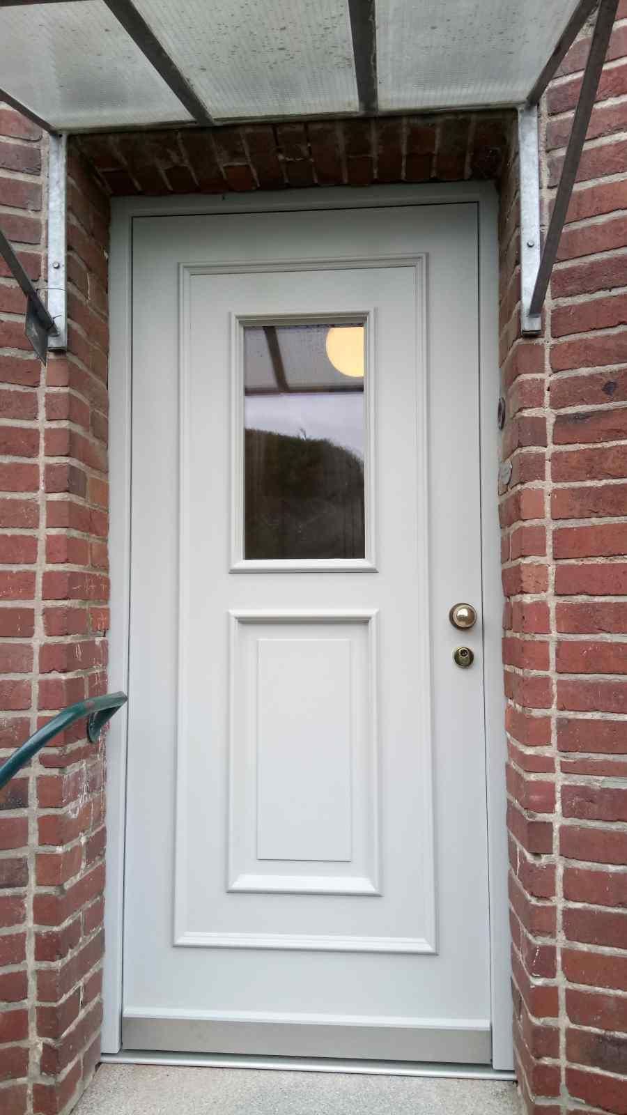 An einem Backsteingebäude befindet sich eine weiße Tür mit einem Glasfenster.